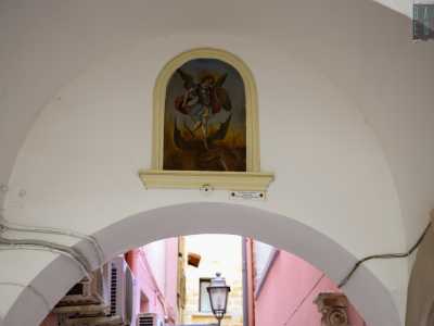 Arrivati sotto l�Arco del Vico ci basta alzare lo sguardo per trovarci davanti all�edicola dell�Arcangelo Michele, l�unica di Palo che rappresentano un santo, incastonata nel muro bianco. L�iconografia � quella tradizionale: Michele schiaccia con un piede il demonio mentre in una mano regge uno scudo con una grande croce